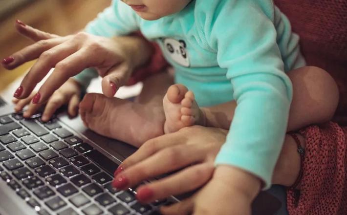 أم مع طفلها خلال قيامها بالكتابة على لوحة مفاتيح جهاز كمبيوتر محمول - المصدر: بلومبرغ