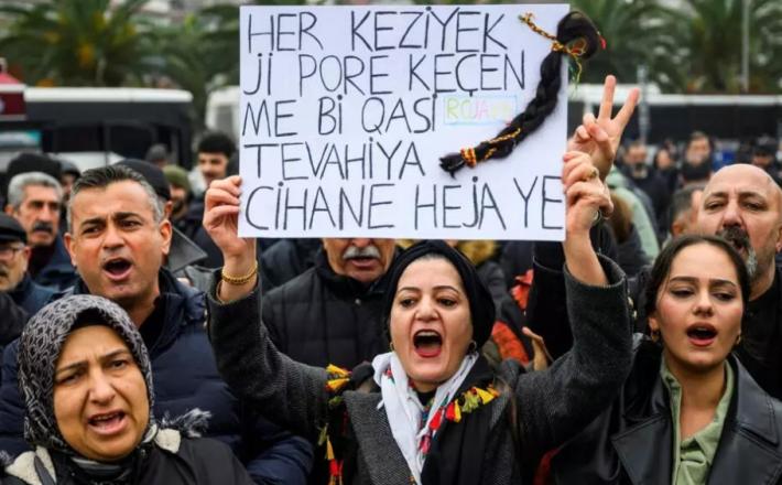 رفعت متظاهرة لافتة كُتب عليها "كل شعرة في رؤوسنا ثمينة كالعالم أجمع"، مع ضفيرة شعر مُعلقة بها، وهي تُردد شعارات خلال مظاهرة تضامنية مع الأكراد في شمال سوريا، في إسطنبول، بتاريخ 24 يناير/كانون الثاني 2026. AFP - YASIN AKGUL